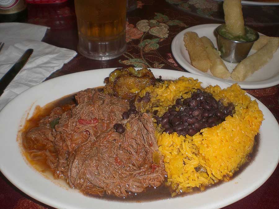 Uma refeição tradicional de ropa vieja (fraldinha desfiada à base de molho de tomate), feijão preto, arroz amarelo, banana da terra e mandioca frita